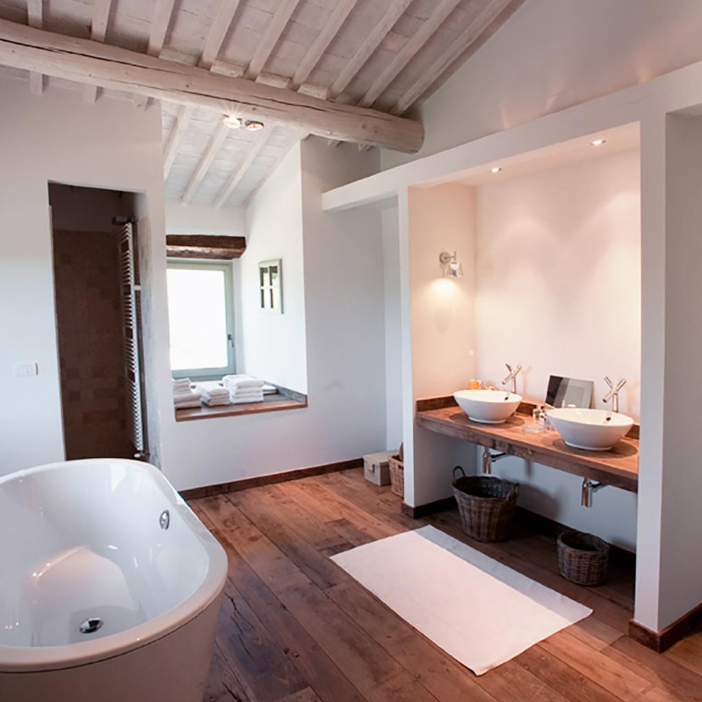 Modern bathroom with freestanding bathtub, double sinks, wooden floors, and exposed beam ceiling, designed by Archidomus, Architect Monica Rossi.