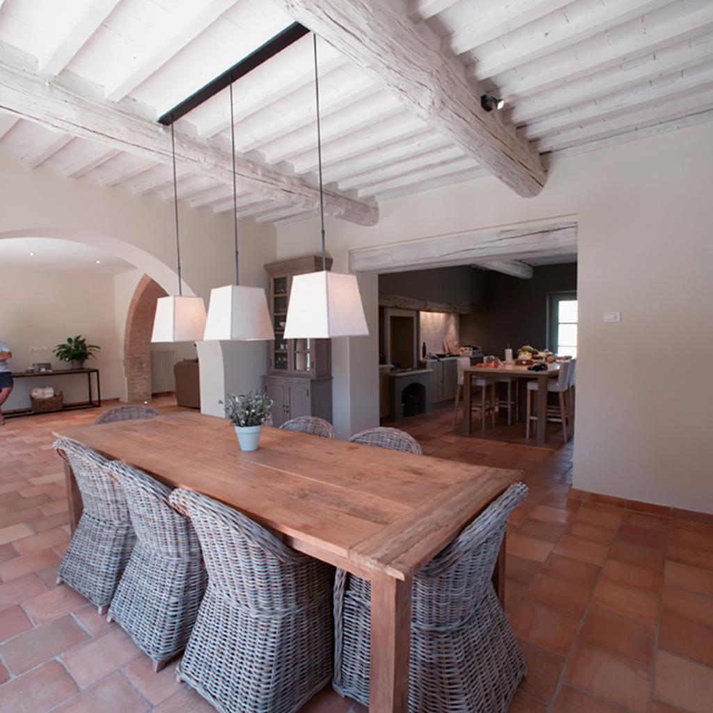 Rustic dining room with wooden table, wicker chairs, terracotta tile flooring, and exposed beam ceiling, designed by Archidomus, Architect Monica Ros