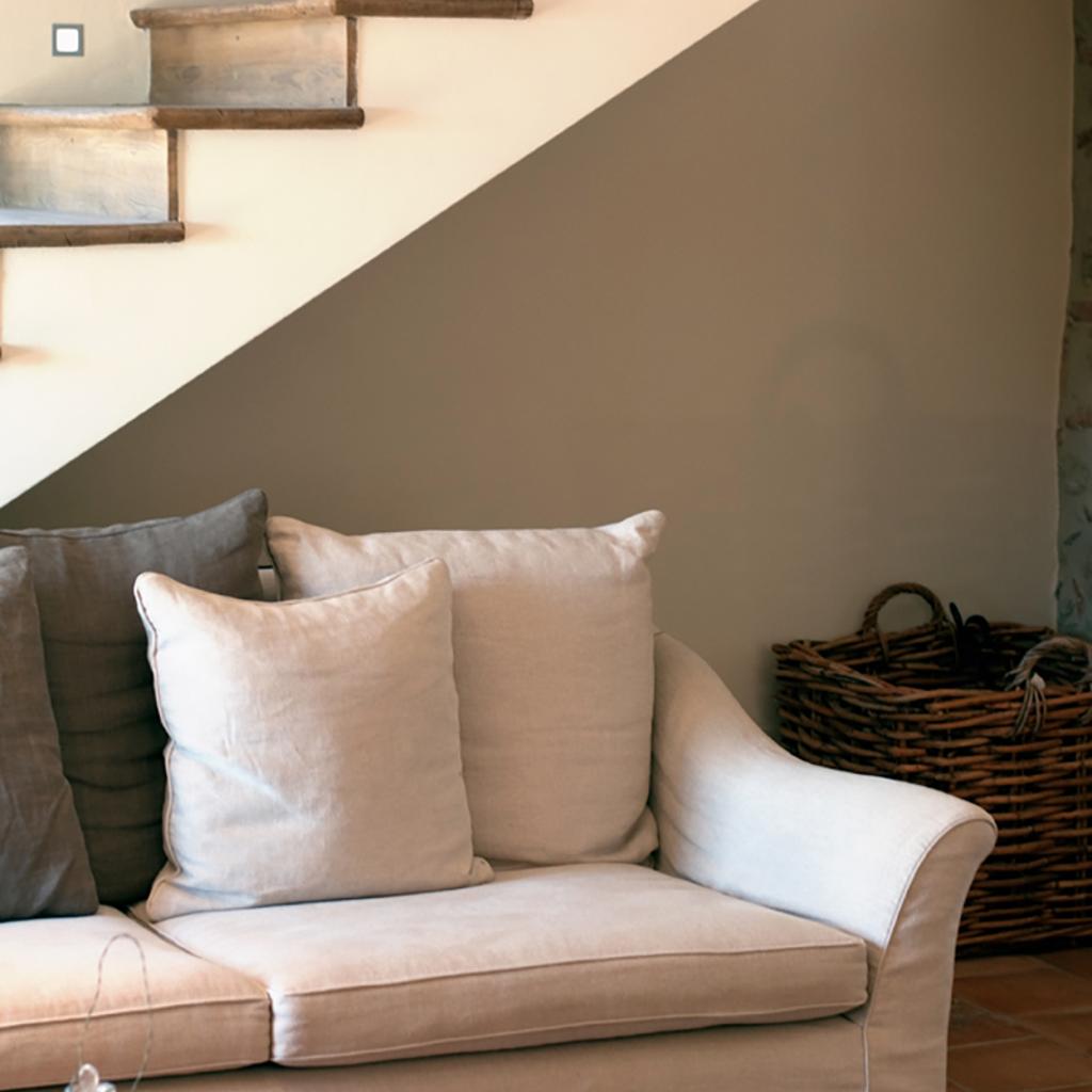 Wooden staircase next to a sofa with grey cushions.