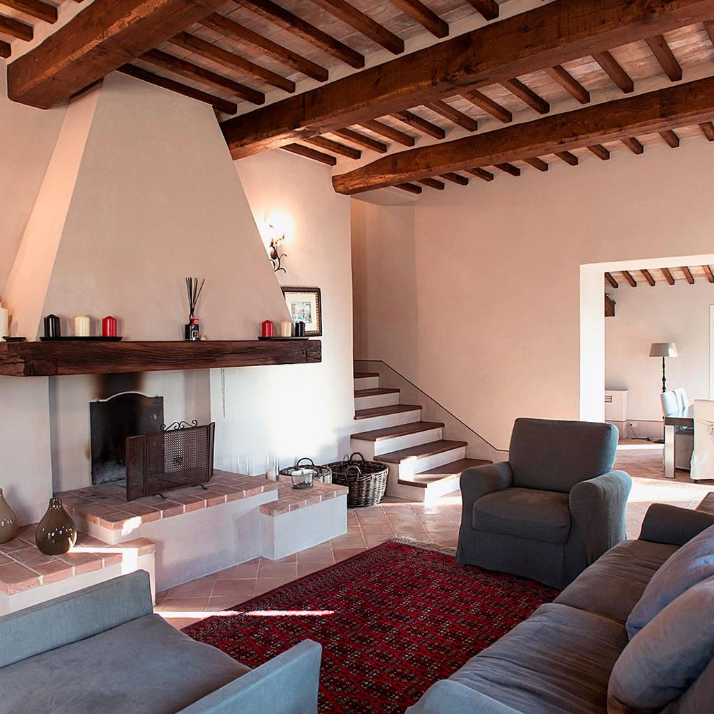 Rustic living room with exposed wooden beams, a fireplace, and cozy seating, designed by Archidomus and Architetto Monica Rossi.