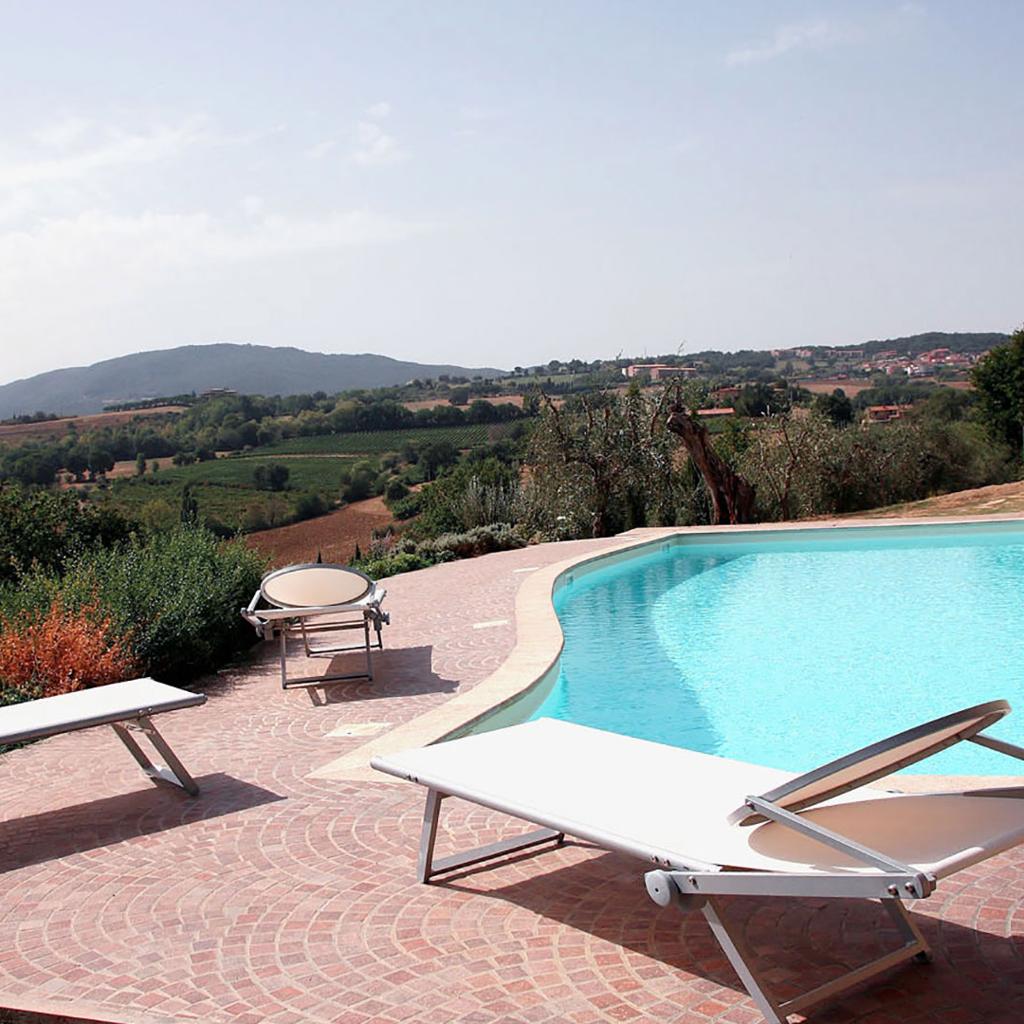 Outdoor swimming pool with lounge chairs and a scenic view of the countryside, designed by Archidomus - Architect Monica Rossi.