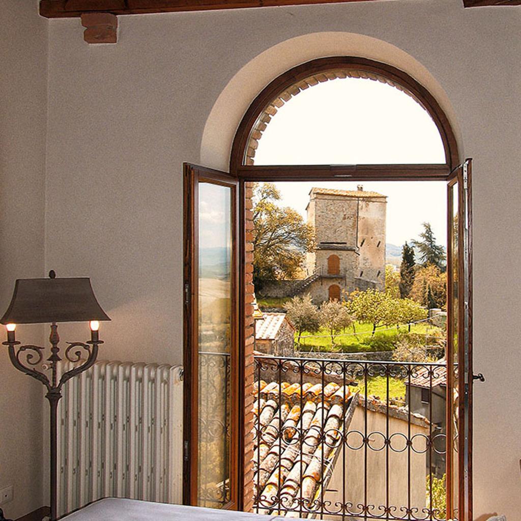 : Vista dalla camera da letto con una finestra ad arco che si apre su un paesaggio con una torre in pietra, realizzata da Archidomus - Architetto Monica Rossi