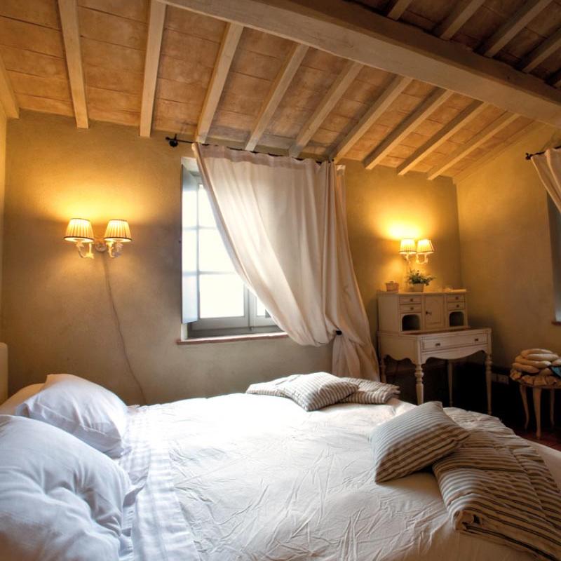 Cozy bedroom with double bed and wooden beam ceiling, house designed by Archidomus - Monica Rossi architect