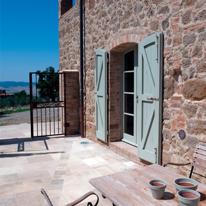 Rustic stone exterior with green shutters, wooden outdoor furniture, and tiled patio, designed by Archidomus, Architect Monica Rossi.