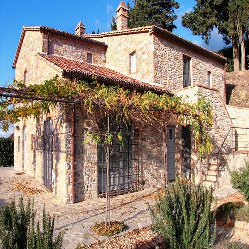 Rustic stone house with terracotta roof, arched windows, and pergola with climbing plants, designed by Archidomus, Architect Monica Rossi.