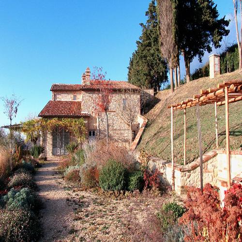 Rustic stone house with terracotta roof, arched windows, landscaped garden, and pergola, designed by Archidomus, Architect Monica Rossi.