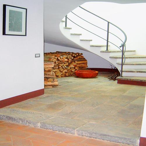 : Modern stairway with curved design, stone floor, and stacked firewood. Created by Archidomus - Monica Rossi Architect.