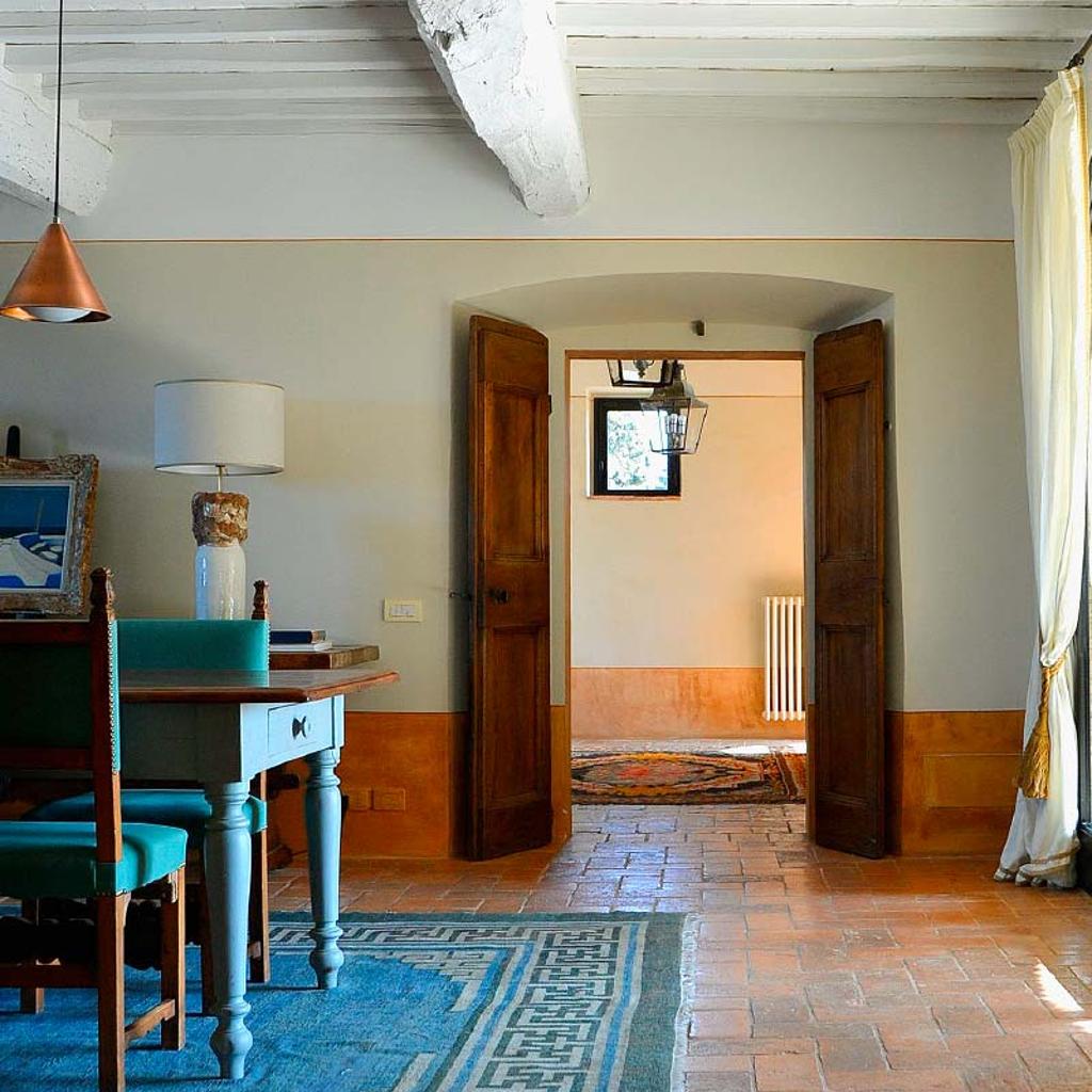 Interno di una casa rustica con travi in legno e porte aperte, progettato da Archidomus architetto Monica Rossi.