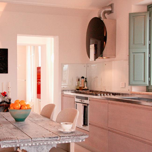 Modern kitchen designed by Archidomus, featuring a rustic dining table with a bowl of oranges, sleek cabinetry, and a minimalist decor by Architetto Monica Rossi.